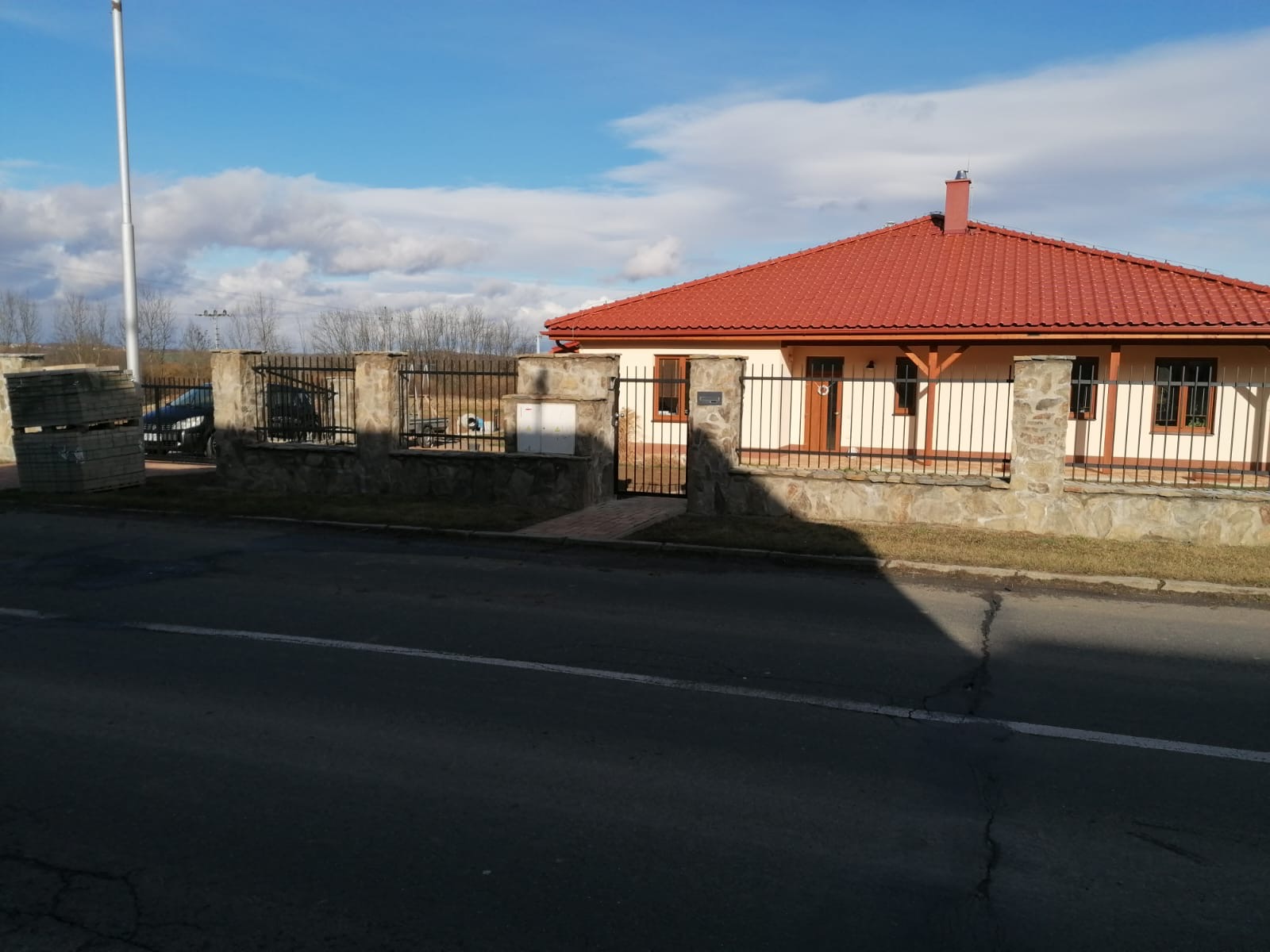 Plot z kamenných sloupků s kovovou brankou u domu